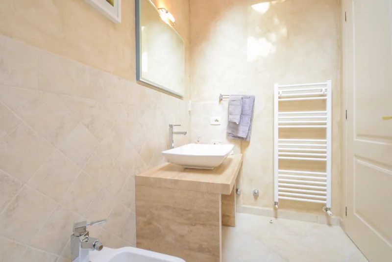 Bathroom with light-coloured tiles, washbasin, window and heated towel rail