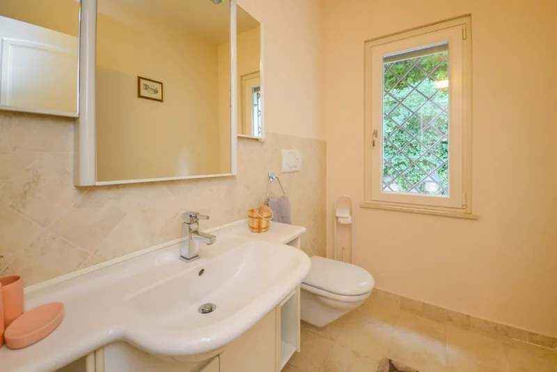 Bathroom with a shaped washbasin, large mirror and window overlooking greenery